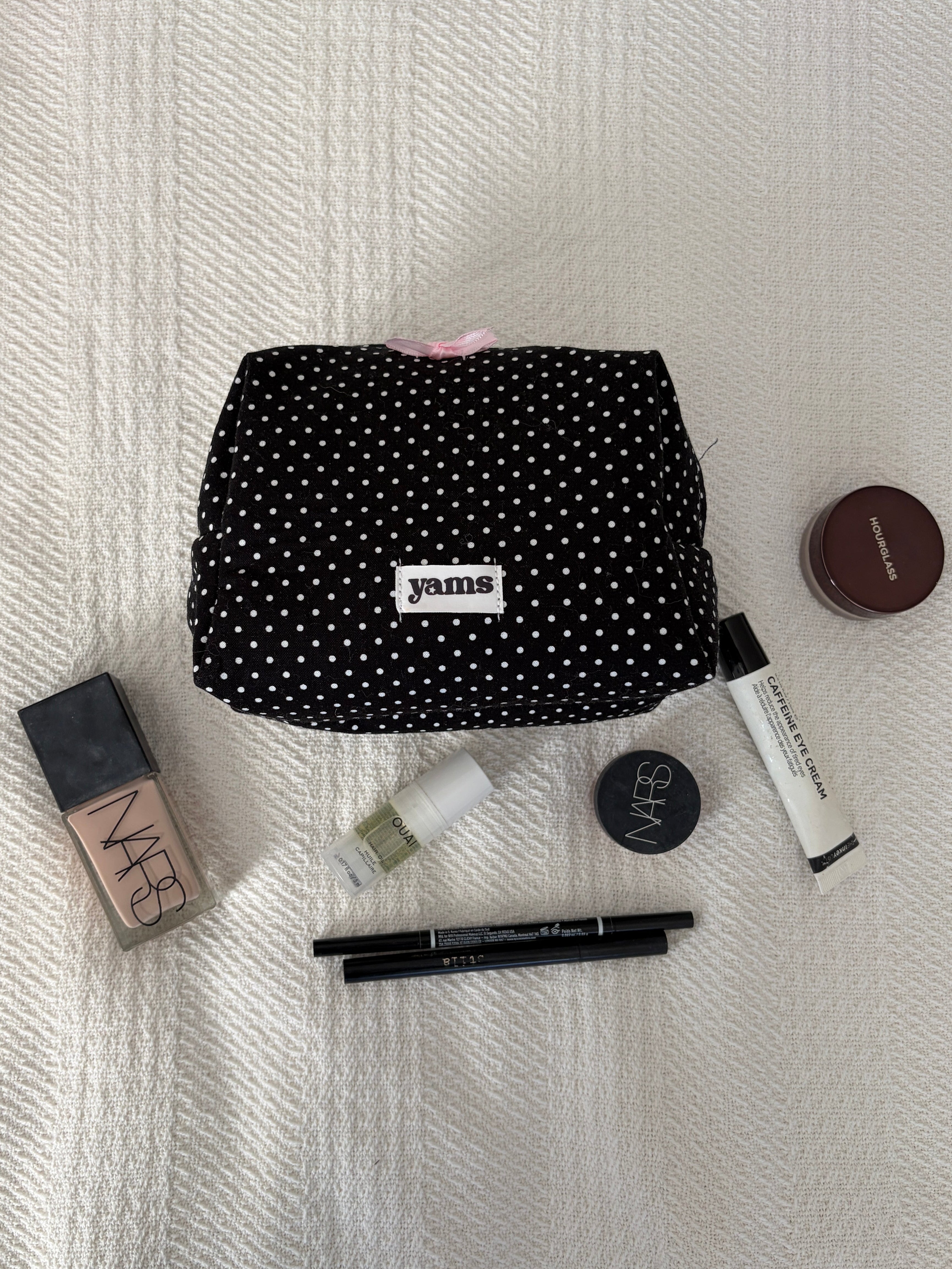 Black polka dot makeup bag with cosmetic items on a white textured surface